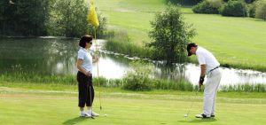 Female holding the the flag while the male gets ready to putt