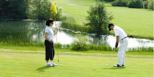 Female holding the the flag while the male gets ready to putt