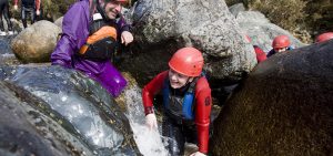 Guys climbing between rocks through the river